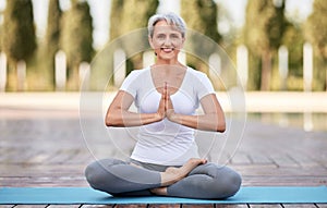 Calm happy mature woman sitting in lotus pose on mat during morning meditation in park