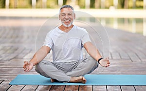 Calm happy senior man sitting in lotus pose on mat during morning meditation in park