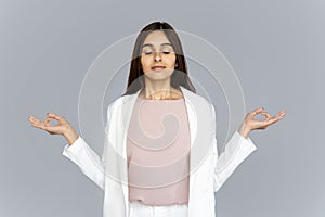 Calm healthy indian business woman meditating on grey studio background