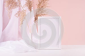 Calm home decor with blank photo frame for text, silk curtain, fluffy reeds bouquet on white wood table, pink wall. Template.