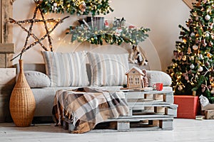 Calm image of interior modern home living room decorated christmas tree and gifts, sofa, table covered with blanket.