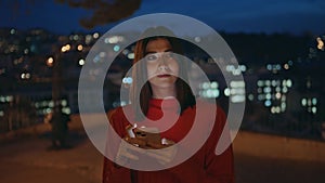 Calm lady holding smartphone walking night with blurred city background closeup