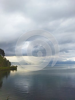 a calm lake under a cloudy skysunlight penetrates the clouds
