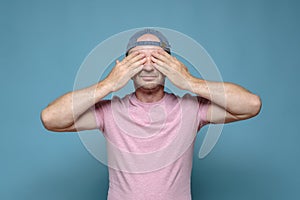 Calm man in a cap and a pink T-shirt covered his eyes with hands, he expects a surprise or does not want to see