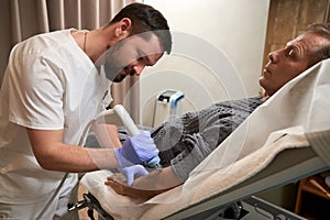 Calm man on hospital bed having his arm treated with shockwave therapy