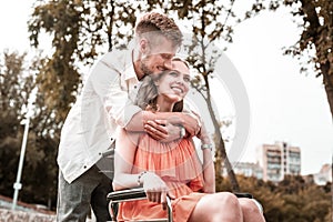 Calm man smiling and hugging girlfriend in wheelchair