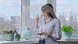 Calm mature woman drinking coffee, looking out the window at home