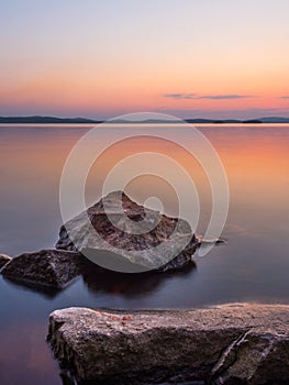 Calm and meditation concept. Sunset on the lake, rocks in the foreground, quiet water, cloudless sky