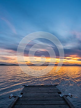 Calm and meditation concept. Sunset on the lake, wooden bridge in the foreground, quiet water, cloudless sky