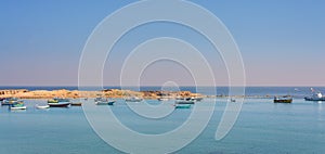 Calm Mediterranean sea with clear sky, small boats and small island at the coast of Alexandria, Egypt