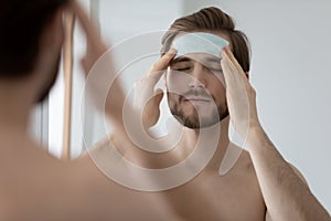 Calm metrosexual millennial man applying cleansing patch on forehead photo