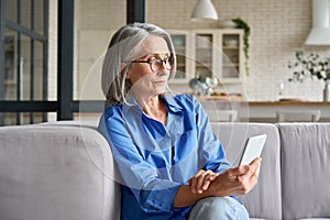 Calm mid age 60 woman at home using cellphone reading watching online video.