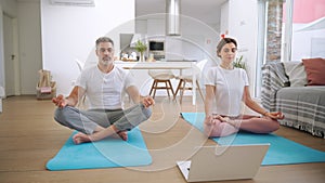 Calm middle aged couple learning online yoga meditating using laptop at home.