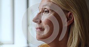 Calm middle-aged woman staring out window look pensive, closeup