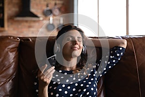 Calm millennial woman in headphones listen to music on cell