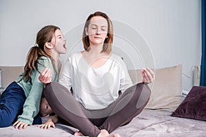 Calm mindful single mom doing yoga at home while active noisy kid daughter screaming in her ear, mother meditating for stress