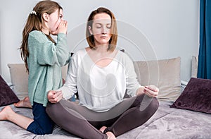 Calm mindful single mom doing yoga at home while active noisy kid daughter screaming in her ear, mother meditating for stress