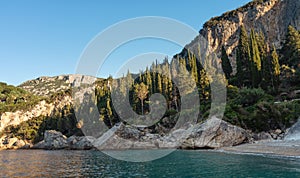 Calm morning sea near rough sand beach at Liapades Corfu, Greece - sun shines on hills with coniferous trees background