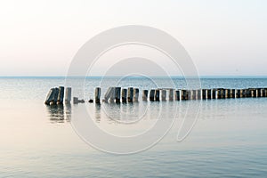 Calm morning sea surface with old stone pier and rocks