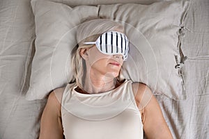Calm old woman enjoying sleep wear sleeping mask in bed