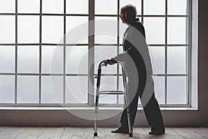 Calm old woman holding foldable walker in room of clinic photo