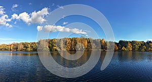 Calm panoramic countryside landscape with quiet river and motley autumn colorful forest after it under blue sky with clouds