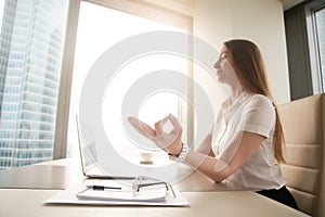 Calm peaceful businesswoman practicing yoga at work, meditating