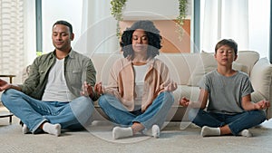 Calm peaceful multiracial family African American parents teach meditation son kid with closed eyes do yoga exercise mom