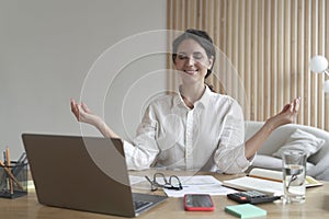 Peaceful woman freelancer meditating and doing breathing exercises after hard working day at home