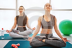 Calm and peaceful young women sit on matrass and meditate. They keep eyes closed and hold heads up. Models sit on lotis