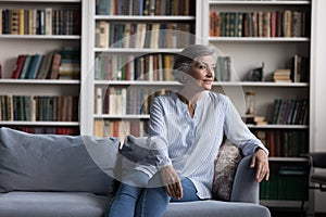 Calm pensive aged woman sit on sofa in living room photo