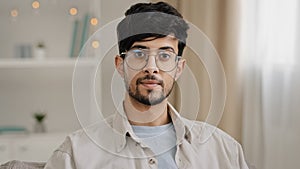 Calm portrait close-up bearded face millennial arabic indian man guy with glasses looking at camera smiling waving nods
