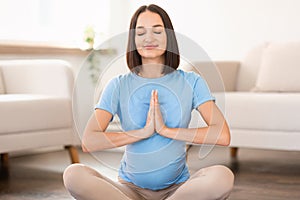 Calm pregnant lady practicing prenatal yoga with eyes closed indoor