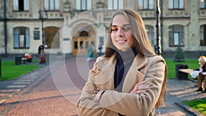 Calm and pretty caucasian model female is standing with her hands crossed and looking happily at camera while being