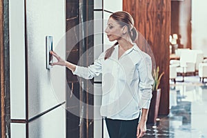 Waist up of calm long haired woman pushing the elevator button