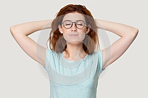 Calm red-haired girl relax in studio hands over head