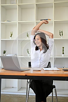 Calm and relaxed Asian businesswoman stretching her arms at her desk