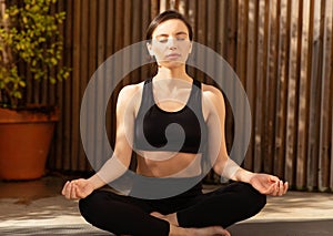 Calm relaxed millennial european woman athlete in sportswear practicing yoga in city, meditating
