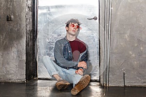 Calm relaxed model man in bright red sunglasses and denim casual style, sitting near metallic door,
