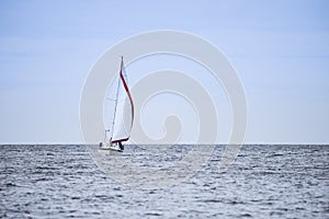 Calm relaxing image of sailing boat in soft blue sky with red sa