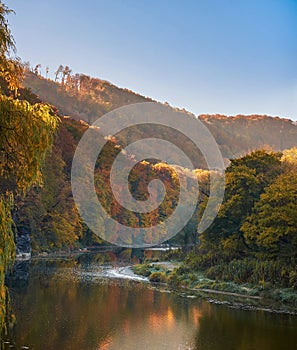 The calm river flows among the foxed hills on a sunny autumn morning