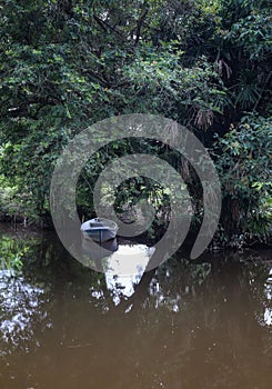 calm river water with small and old fishing boat park under the tree branches photo