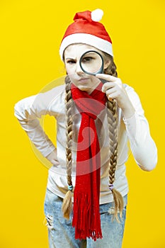 Calm Scrutinizing Caucasian Girl in Santa Hat And Red Scarf Holding Empty Big Magnifying Glass While Searching and Posing on