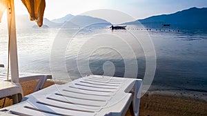 Calm sea surface and empty sunbeds on the sea beach at sunrise