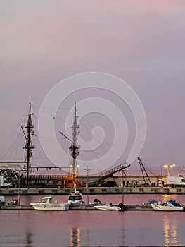 Calm sea water and sunset pink reflections on the harbor. Water landscape with boats