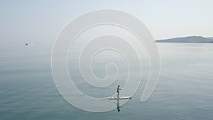 Calm seascape. Man moving on sup board. Boats floating on horizon in distance