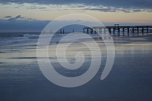 Calm seascape with a pier and splashing waves at soft sunset