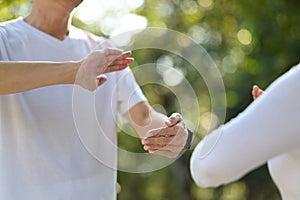 Calm senior woman with eyes closed meditating or practicing traditional Tai Chi Chuan in nature.