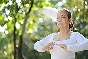 Calm senior woman with eyes closed meditating or practicing traditional Tai Chi Chuan in nature.