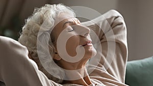 Calm senior woman relax on sofa breathing fresh air